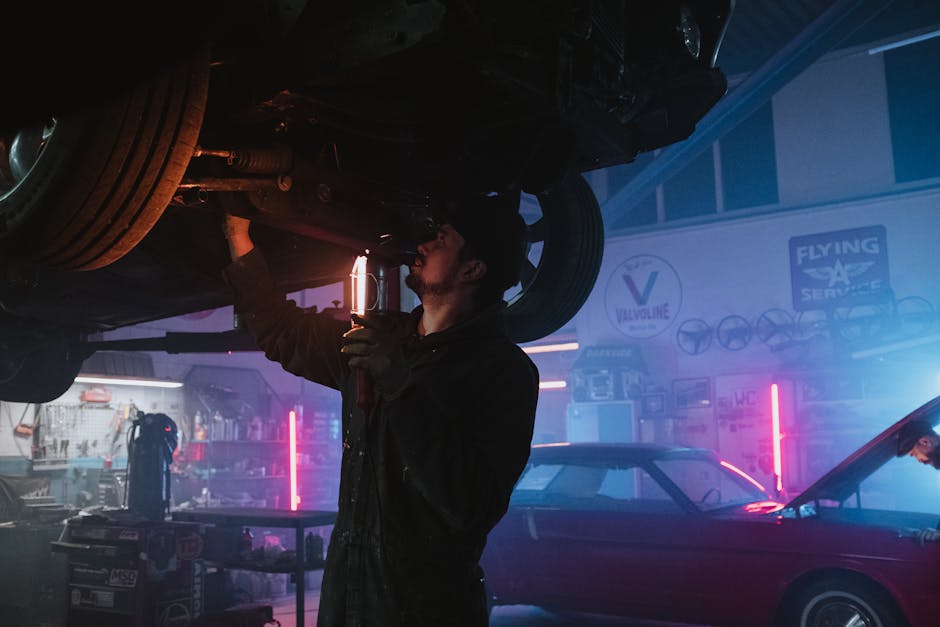 A mechanic inspects a car's undercarriage in a vibrant, neon-lit garage setting, highlighting automotive repair work.